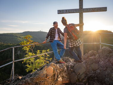 Zwei Wanderer auf dem Aschenbergstein mit Gipfelkreuz, im Hintergrund ist der Inselsberg zu sehen